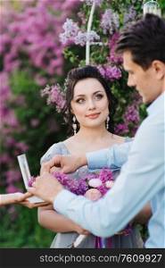 the groom dresses the bride with wedding rings near the lilac arch