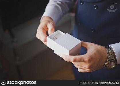 The groom holds an open white box with wedding rings in his hands.. An open box with wedding rings in the hands of the groom 2620.