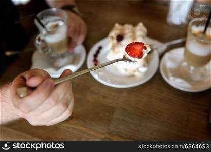 the groom holds the spoon meringue with strawberries on the background of the table with coffee