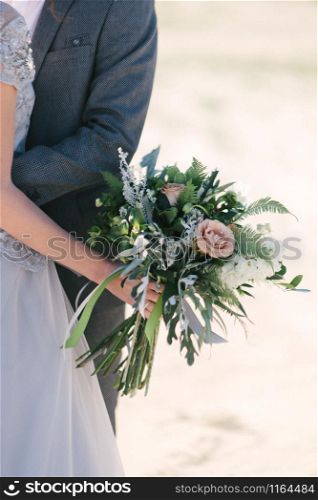 The groom in a suit hugs the bride in a wedding dress close up. The groom in a suit hugs the bride in a wedding dress