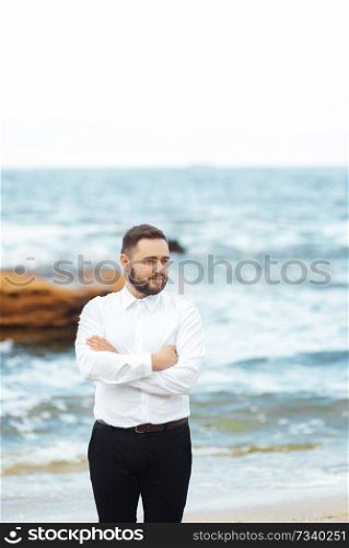 the groom in a white shirt and black pants stands on the beach