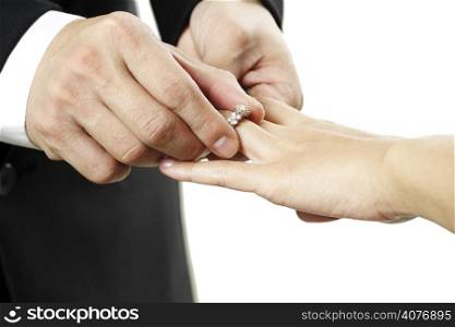 The groom inserting a diamond ring into the bride&acute;s finger