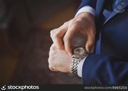 The grooms hands adjust the time on the hand watch.. A man in a suit looks at the time on his watch 2617.