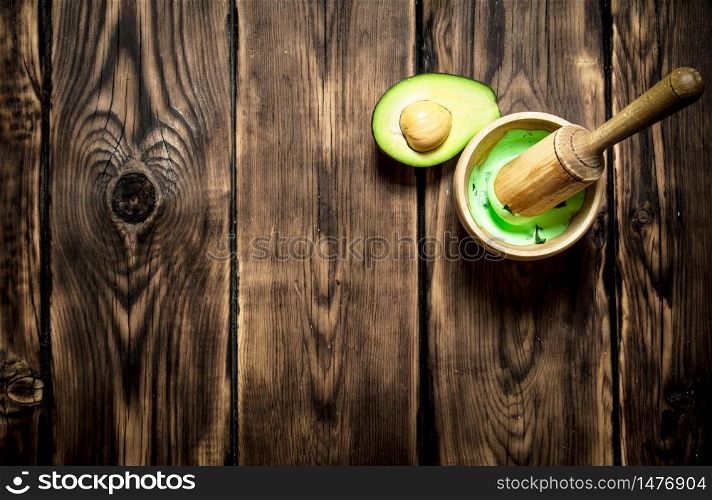 The guacamole in a mortar with pestle. On wooden background.. The guacamole in a mortar with pestle