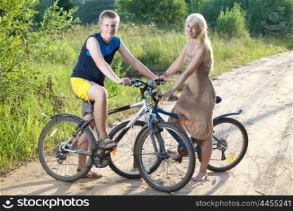 The guy and the girl by bicycles on the rural road in the summer evening