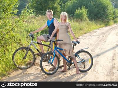 The guy and the girl by bicycles on the rural road in the summer evening