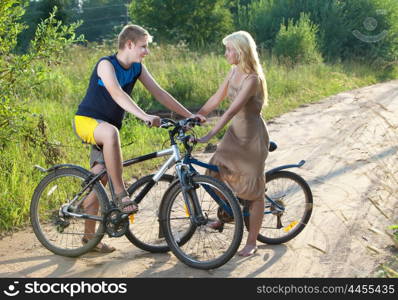 The guy and the girl by bicycles on the rural road in the summer evening