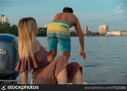 The guy jumps into the water from the boat. A beautiful girl is watching him. Khabarovsk, Russia - Jul 19, 2019: The guy jumps into the water from the boat. A beautiful girl is watching him.