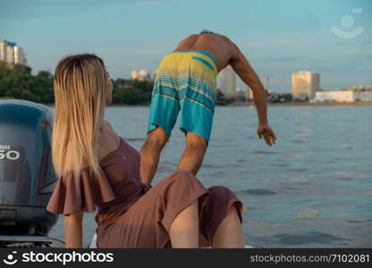 The guy jumps into the water from the boat. A beautiful girl is watching him. Khabarovsk, Russia - Jul 19, 2019: The guy jumps into the water from the boat. A beautiful girl is watching him.