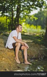 The guy sitting on the shore of the pond.. Portrait of a young man sitting on the beach 6345.