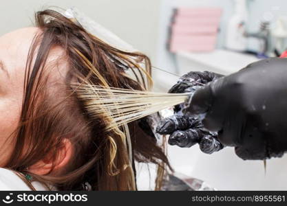 The hairdresser in black gloves paints a brunette woman’s hair in the beauty salon close. The hairdresser in black gloves paints a brunette woman’s hair in the beauty salon.