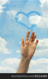 The hand draws on wet glass on a background of clouds. Love in clouds
