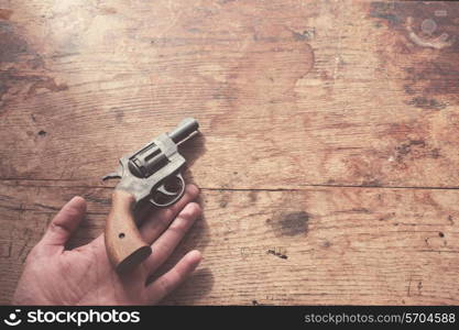 The hand of a man is holding a gun at a wood table