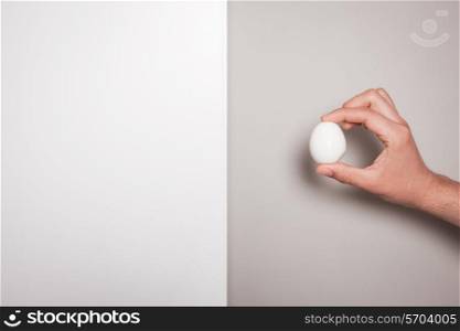 The hand of a man is holding an egg against a dual colored background