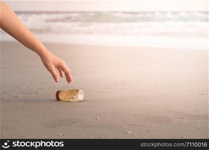The hand of a woman is picking up a plastic bottle to clean the beach.