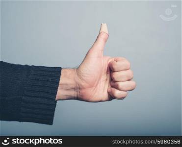 The hand of a young man is gesturing thumbs up with a plaster covering a wound on his thumb
