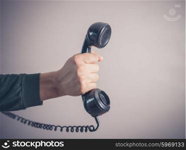 The hand of a young man is holding a vintage rotary telephone