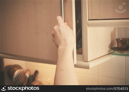 The hand of a young woman is opening a kitchen cupboard