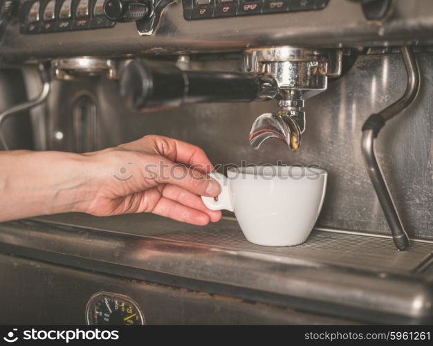 The hand of a young woman is operating a professional coffee machine