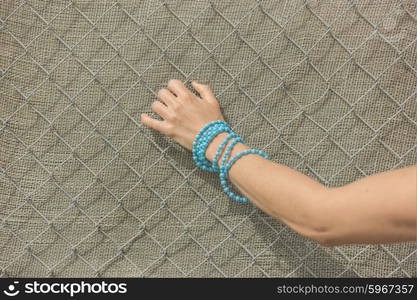 The hand of a young woman wearing a blue bracelet is grabbing a fence outside