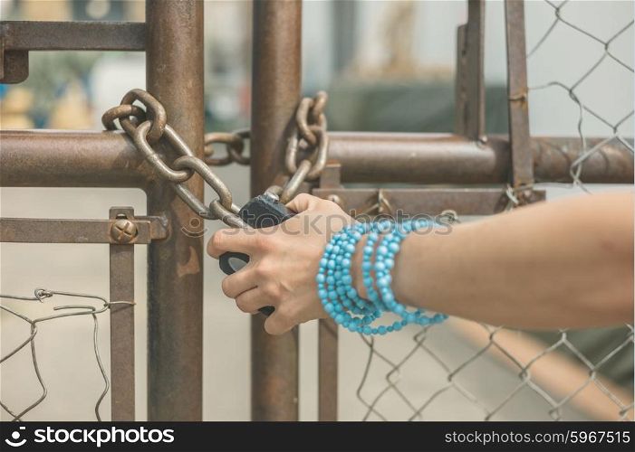 The hand of a young woman wearing a blue bracelet is grabbing a padlock outside