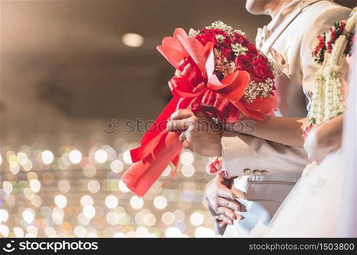 The hand of the bride and groom. Red roses bouquet at a party celebrating the wedding with beautiful bokeh background.
