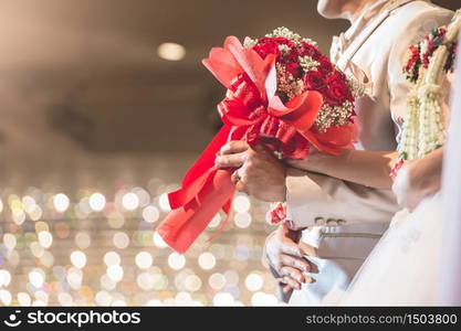 The hand of the bride and groom. Red roses bouquet at a party celebrating the wedding with beautiful bokeh background.