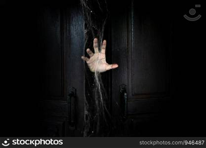 The hand of the man holding the stick from the wooden door from the inside of the dark room