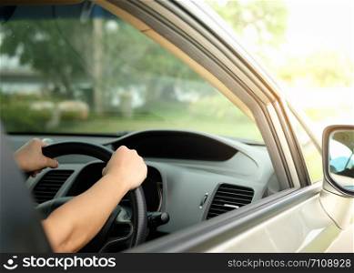 The hands are holding the steering wheel and driving on a light day.