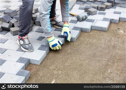 The hands of a bricklayer in protective gloves lay out a pattern of paving slabs on a sandy base on the sidewalk. Copy space, selective focus.. A gloved worker lays the paving slabs observing the required pattern. Copy space.