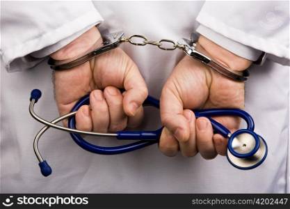 the hands of a doctor with a stethoscope and handcuffs