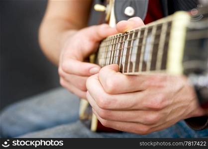 The hands of a sitting guitarist on the fingerboard. Selective focus on the musicians left hand