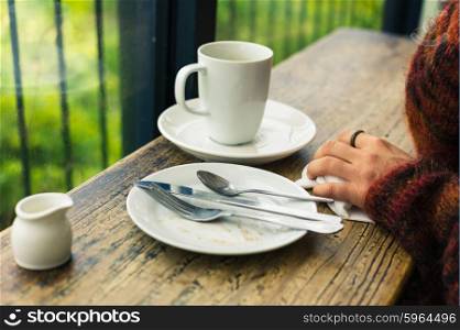 The hands of a woman as she is cleaning up empty plates and a mug in a cafe