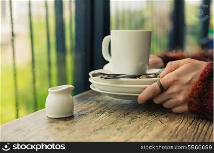 The hands of a woman as she is cleaning up empty plates and a mug in a cafe