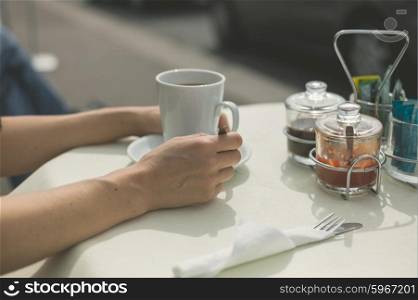The hands of a woman resting on a table outside as she is drinking coffee