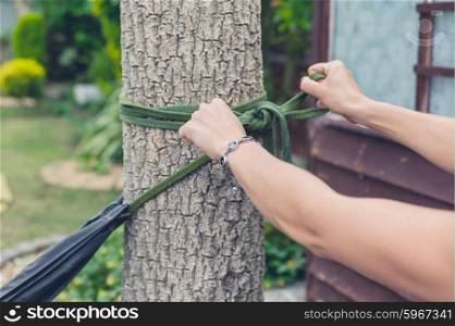 The hands of a young woman as she is tying a hammock to a tree in a garden