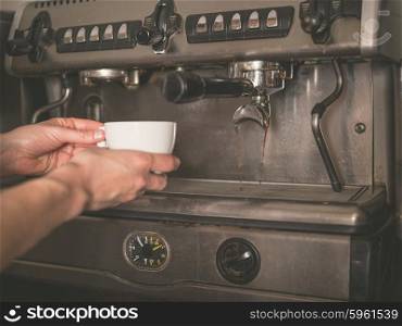 The hands of a young woman is placing a cup under the dispenser of a professional coffee machine