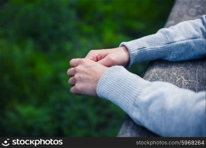 The hands of a young woman resting on a wooden beam outside