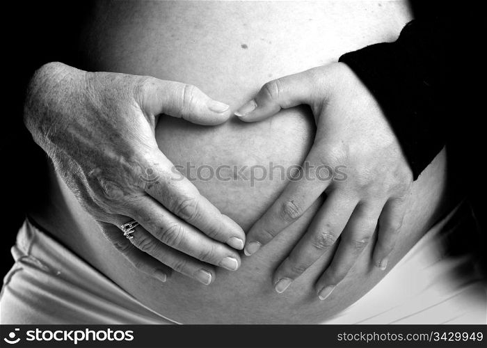 The hands of both future grandmother and future mother on the hands on a pregnant belly. The old and young hand figure a heart. Old and young hand on pregnant belly