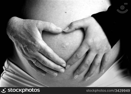The hands of both future grandmother and future mother on the hands on a pregnant belly. The old and young hand figure a heart. Old and young hand on pregnant belly