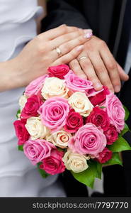 the hands of the bride and groom lying on the bridal bouquet