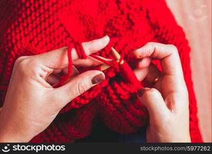 The hands that hold needles and knitting a red warm jacket. Female hands knits sweater