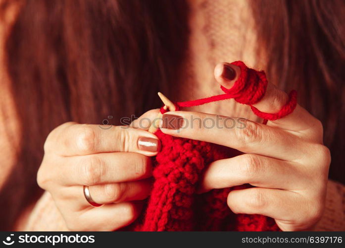 The hands that hold needles and knitting a red warm jacket. Female hands knits sweater