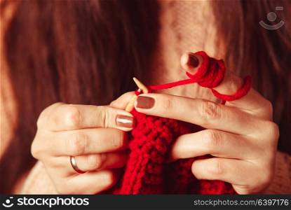 The hands that hold needles and knitting a red warm jacket. Female hands knits sweater