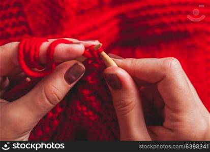 The hands that hold needles and knitting a red warm jacket. Female hands knits sweater