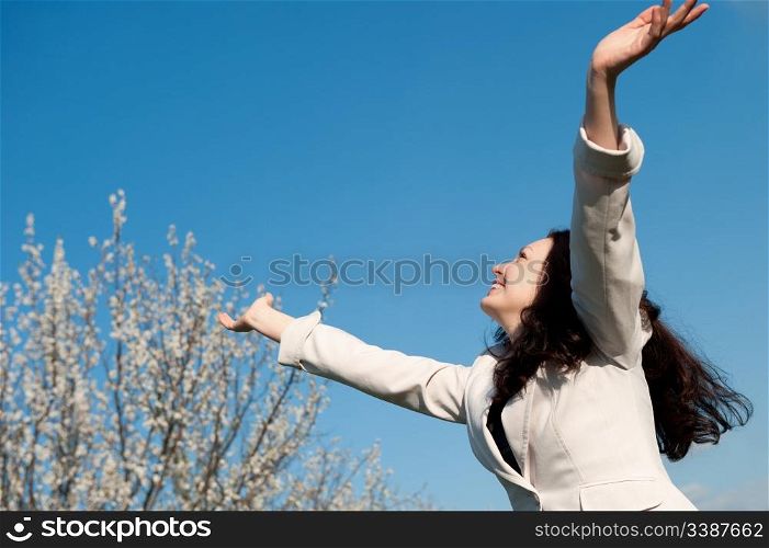 The happy attractive woman with the lifted hands. Against the blue sky