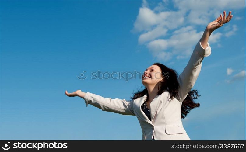 The happy attractive woman with the lifted hands. Against the blue sky