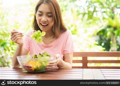 The happy beautiful Asian healthy middle aged woman sitting in the balcony of the house beside the garden and eat a healthy green salad. Concept of health care and nutritious food