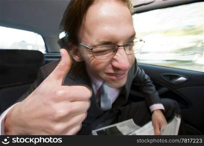 The happy businessman in the backseat leaning forward giving a thumbs-up while winking. Motion blur with fill flash on the rear curtain.