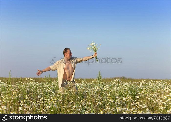 The happy young man in the field with a bouquet of camomiles